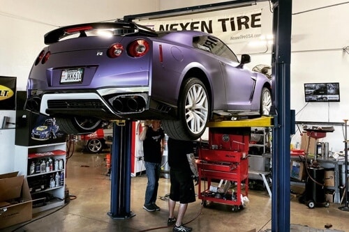 3 Simple Steps You Can Take to Help Prevent Expensive Auto Repair in Gilbert AZ with Ace Performance Automotive; image of purple sedan up on lift in shop bay with our 2 mechanics performing auto repair underneath