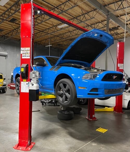 maintenance services image of blue mustang with hood open on lift in shop bay