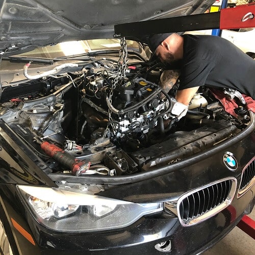 About Us | Ace Performance Auto in Gilbert, AZ & Queen Creek, AZ. Image of a car mechanic doing auto repair on a black BMW.