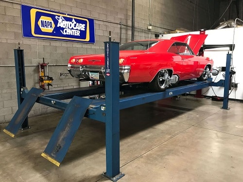 About Us | Ace Performance Auto in Gilbert, AZ & Queen Creek, AZ. Image of a red vintage car undergoing wheel alignment in an auto garage shop. With the banner "NAPA Auto Care Center" in the background. 
