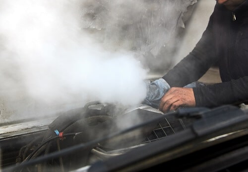 Cooling System Service in Gilbert, AZ | Ace Performance Auto. Image of a man mechanic repairing a smoking engine of an overheated car.
